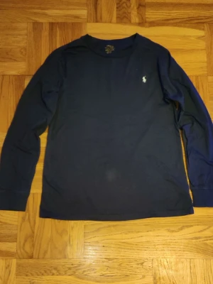 Mörkblå långärmad topp Polo Ralph Lauren - Klassisk mörkblå långärmad topp från Polo Ralph Lauren med rund halsringning och den ikoniska loggan broderad på bröstet. Perfekt för en stilren och enkel look.