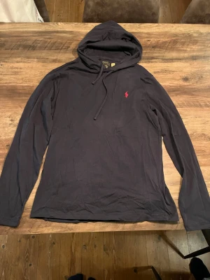 Svart hoodie från Polo Ralph Lauren - Marinblå hoodie från Polo Ralph Lauren med klassisk röd logga broderad på bröstet. Tillverkad i mjuk, tunn bomull, har långa ärmar och dragsko i huvan.