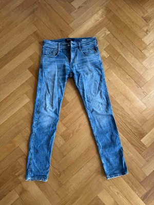 Blå Replay jeans med smal passform - Snygga blå jeans från Replay med klassisk femficksdesign och smal passform. Jeansen har en ljus tvätt och subtila slitningar för en trendig look. Perfekta för dig som gillar stilrena och bekväma jeans.