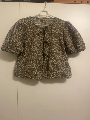 Leopardmönstrad blus med puffärm - Snygg blus med leopardmönster och puffiga korta ärmar. Blusen har rund halsringning och knytning framtill. Perfekt för dig som vill sticka ut med ett djurmönstrat plagg. Materialet känns mjukt och bekvämt.