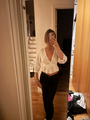 Vit omlottopp med volang och spets - Snygg vit omlottopp med djup v-ringning, trekvartsärm och volang nertill. Toppen har broderade spetsdetaljer och är croppad, perfekt till höga jeans eller kjol. Luftigt material som passar bra till varmare dagar.