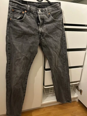 Levi's 501 grå jeans straight fit - Grå Levi's 501 jeans med klassisk straight fit och knappgylf. Jeansen har fem fickor, tydliga sömmar och den ikoniska läderpatchen bak. Tillverkade i slitstark bomullsdenim med vintagekänsla och snygg tvätt.