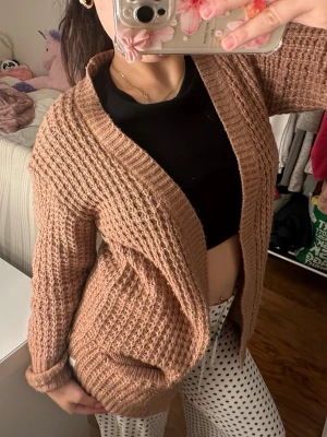 Brun stickad kofta med grov struktur - Mysig brun stickad kofta med öppen front och grovstickad struktur. Koftan har långa ärmar och bred ribbad kant längs öppningen. Perfekt att slänga på sig över en t-shirt för en avslappnad look.