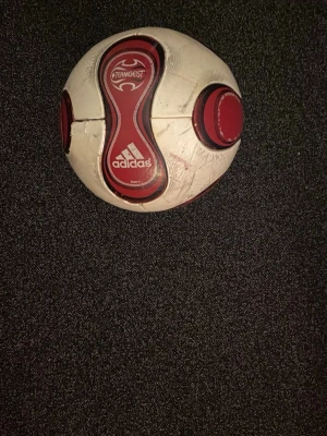 Adidas Teamgeist fotboll röd/vit - Säljer en Adidas Teamgeist fotboll i storlek 5. Bollen är vit med röda och svarta detaljer och har den klassiska Teamgeist-designen. Perfekt för fotbollsträning eller match. Adidas-logga och Teamgeist-tryck syns tydligt.