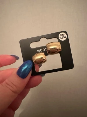 Guldiga chunky örhängen från Montini - Säljer ett par chunky örhängen i guldig metall från Montini. De har en rundad, bred design som ger en trendig och stilren look. Perfekta för dig som gillar statement-smycken och vill addera lite extra bling till din outfit.