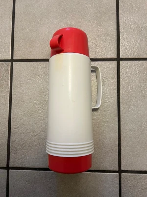 Röd och vit termos från AB Termoform - Säljer en klassisk termos i plast från AB Termoform, tillverkad i Sverige. Termosen är vit med röda detaljer på locket och botten samt har ett praktiskt handtag på sidan. Perfekt för att ta med varm dryck på utflykten eller till jobbet.