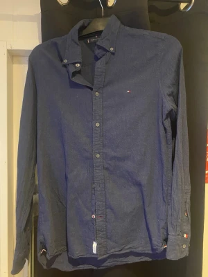 Mörkblå skjorta Tommy Hilfiger S - Säljer en mörkblå slim fit skjorta från Tommy Hilfiger i storlek S. Skjortan har klassisk button-down krage, små logodetaljer på bröstet och ärmarna samt knappar framtill. Tillverkad i mjuk bomull och har långa ärmar. Perfekt till jeans för en clean look.