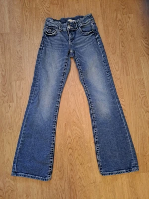Blå bootcut jeans med klassisk look - Snygga blå bootcut jeans med klassisk femficksdesign och normal passform. Jeansen har en lätt tvättad look och raka ben som blir vidare nedtill. Perfekta för dig som gillar en avslappnad men ändå stilren vibe. Storlek 158 cl motsvarande 34.