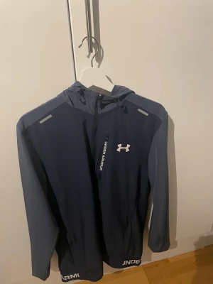 Blå vindjacka från Under Armour - Typ helt ny. Använt 1 gång. Säljer då den inte passar min stil längre. Köpt för ca 2 månader sen 