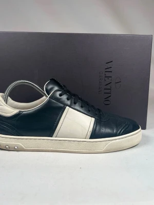 Valentino Garavani svartvita sneakers - Snygga sneakers från Valentino Garavani i svart och vitt skinn. Klassisk låg modell med rund tå, snörning och små nitar på sidan av sulan. Sulan har ett unikt mönster undertill och skon har en stilren design som sticker ut.