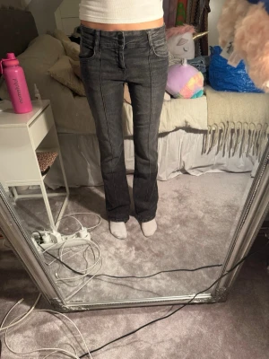 Grå bootcut jeans med kontrastsömmar - Säljer ett par gråa bootcut jeans med tydliga kontrastsömmar framtill. Jeansen har normal passform och klassisk femficksdesign. Materialet är jeans i bomullsmix och färgen är en snygg tvättad grå ton.