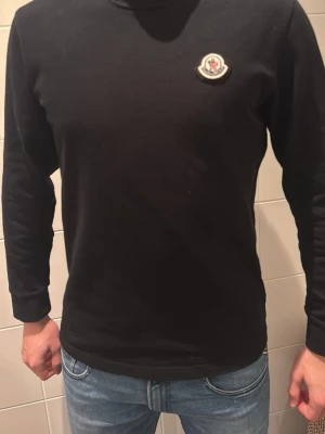 Svart långärmad tröja från Moncler - Svart långärmad tröja från Moncler med rund halsringning och klassisk logotyp på bröstet. Enkel och stilren design som passar perfekt till jeans eller andra byxor. Kvitto finns och tröjan är köpt från NK i Stockholm. Först till kvarn!