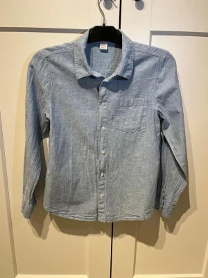 Ljusblå skjorta i linne från Uniqlo - Snygg ljusblå skjorta från Lindex i mjukt linne. Klassisk krage, bröstficka och knappar framtill. Perfekt för en avslappnad men stilren look. Långärmad och med en rak passform som funkar till det mesta. Storleken är 158, men funkar som en smäck för XS 