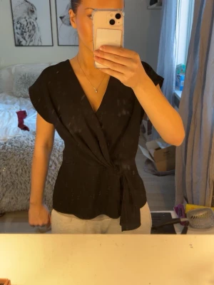 Svart topp med omlottdetalj från Zara – storlek XS - Svart topp från Zara i storlek XS. Använd väldigt sparsamt och i fint skick. Säljer eftersom den aldrig används.  Perfekt både till vardags och jobb 