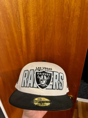Las Vegas Raiders keps från New Era - Snygg Las Vegas Raiders keps från New Era 59FIFTY-serien. Kepsen är beige med svart platt skärm och broderade loggor på fram-, bak- och sidor. NFL-märke på sidan och klassisk Raiders-text framtill. Perfekt för dig som älskar amerikansk fotboll och streetwear.