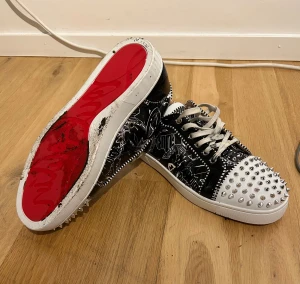 Christian Louboutin sneakers med nitar - Unika sneakers från Christian Louboutin med svartvitt grafiskt mönster och vita snören. Skorna är i mycket bra skick, och kan tvättas i samband med köp. Storlek 42 men passar upp t 43. Köpa här på plick, osäker på äkthet därav pris. Box o dustbag medföljer.