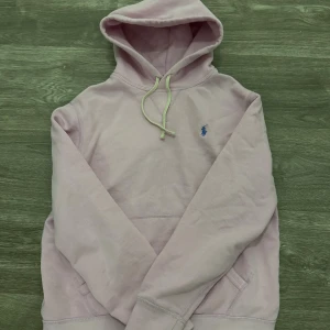 Ljusrosa hoodie från Polo Ralph Lauren - Snygg ljusrosa hoodie från Polo Ralph Lauren med klassisk blå logga på bröstet. Tröjan har huva med snörning och en stor magficka. Tillverkad i mjuk bomull för skön känsla. Perfekt för chill dagar och enkel att matcha med jeans eller joggers. Den har inga fläckar helt ny använd få gånger 