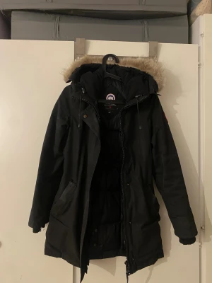  Canada Goose viktoria parkajacka XS - Svart parkajacka från Canada Goose med fluffig päls på huvan och ribbade muddar vid ärmslut. Jackan har dragkedja och knappar framtill, samt praktiska fickor. Perfekt för kalla vinterdagar och har klassisk stil med snygga detaljer. Den är lite sliten men med en kemtvätt blir den nog super igen, det billiga priset då ärmarna är slitna och fickan lite sönder men jag har kunnat använda den ändå utan problem