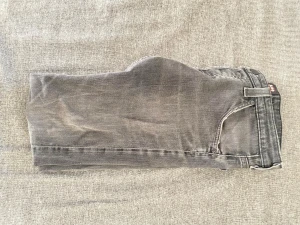 Grå jeans från Lee - Säljer ett par grå jeans från Lee med klassisk femficksdesign och Lee-logga på bakfickan. Jeansen har en rak passform och är tillverkade i mjukt denimtyg. Perfekta för dig som gillar en stilren och avslappnad look.