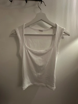 Vit croppad linnetopp med breda axelband - Säljer en vit croppad linnetopp med breda axelband och rundad halsringning. Toppen är ärmlös och har en enkel, stilren design som är lätt att matcha. Materialet känns mjukt och bekvämt, perfekt för varma dagar eller lager-på-lager.