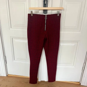 Röd-rutiga leggings från Zara - Snygga röd- och svart-rutiga leggings från Zara med hög midja och silverfärgad dragkedja baktill. Stretchigt mjukt material, sitter tight och är supersköna att bära. Modern punkig look. Funkar perfekt till tisha eller skjorta, och som bas till svart kavaj, eller till lång stickad tröja för att ge mer avslappnad mysfaktor. Modellen på bilderna  är strl 36/S vilket bättre motsvarar passformen än angiven strl M. 
