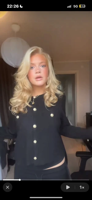 Svart kofta med guldfärgade knappar - Snygg svart kofta med guldfärgade knappar framtill. Koftan har rund hals och lång ärm, perfekt för dig som gillar klassisk stil med en twist. Materialet känns mjukt och koftan har en normal passform som är enkel att matcha med dina favoritjeans.