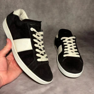 Svarta och vita sneakers från Saint Laurent - Saint Laurent SL02 svarta och vita. Skick 8/10 sulkräm har använts för att fräscha upp skorna lite. Storlek eu 42, inget og. 