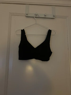Svart bh från Cubus - Svart bh från Cubus i storlek S. Toppen har breda axelband och en snygg v-ringad form framtill. Materialet är mjukt och stretchigt polyester som sitter skönt mot kroppen. Det är paddad men utan bygel.
