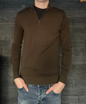 Brun merinoullströja från Sunspel - Snygg brun långärmad tröja från Sunspel i 100% merinoull. Modellen har en half zip vid halsen och sitter normalt på kroppen. Perfekt för dig som gillar stilrena och klassiska plagg med en modern touch.                -Modellen 184cm                                                        -Nypris ca 1300kr