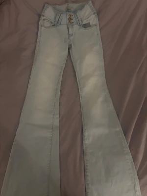 Low waist jeans från infinity Paris  - Snygga ljusblå jeans från Girl VII/infinity Paris med bootcut-modell. Jeansen har tre dekorativa guldknappar framtill, dom är i storlek s men är mer som xs