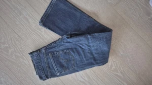 Levi's 505 blå jeans bootcut - Klassiska blå Levi's 505 jeans med bootcut passform. Jeansen har fem fickor, synliga kontrastsömmar och den ikoniska röda Levi's-lappen på bakfickan. Tillverkade i slitstarkt denimtyg som ger en tidlös look.