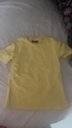 Gul t-shirt från Pieces - Fräsch gul t-shirt från Pieces med klassisk rund hals och korta ärmar. Enkel och stilren design, med slit på båda sidorna 