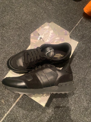 Valentino Rockruners - Svarta Valentino Garavani Rockrunner sneakers med coola camouflagemönster på ovansidan. Skorna har snörning, platt sula med nitar och är tillverkade i en mix av skinn och mocka. Snygg och urban look med rund tå och detaljerad design.