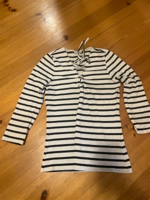 Randig långärmad topp från ONLY - Säljer en vit och svart randig långärmad topp från ONLY i storlek L men sitter som M. Toppen har snörning framtill vid halsen och är ribbad i materialet. Snygg och enkel att matcha med jeans eller kjol, perfekt för dig som gillar en chill och trendig stil.