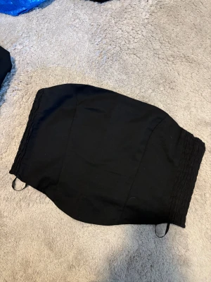 Svart bandeau tubtopp - Säljer en svart bandeau tubtopp med smockade sidor för extra stretch och bekväm passform. Toppen är axelbandslös och har en stilren, enkel design som är lätt att matcha med olika outfits. Perfekt för dig som gillar minimalistisk stil.