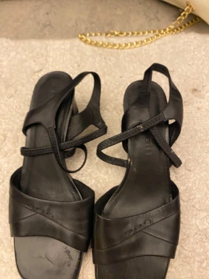 Svarta sandaler i skinn med remmar - Snygga svarta sandaler med korsade remmar och öppen tå. Tillverkade i skinn med minimalistisk design och tunna remmar som ger en stilren look. Perfekta för varma dagar och passar till många outfits.