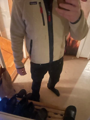 Beige fleecejacka från Patagonia - Säljer en beige fleecejacka från Patagonia med marinblå detaljer och röda dragkedjor. Jackan har hög krage, tre fickor med dragkedja och ett mjukt teddyfoder. Perfekt för kalla dagar och chill häng. Snygg och enkel att matcha. Väldigt bra skick, knappt använd. Vid snabb affär kan pris diskuteras. 