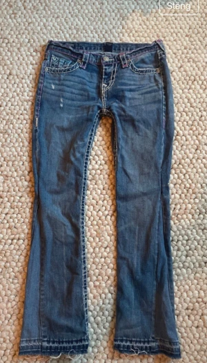 True Religion jeans med färgglada sömmar - OBS!!! Gå in på bilden för att se hela Säljer ett par blå True Religion jeans med kontrastsömmar i rosa, lila och turkos. Jeansen har låg midja, raka ben och slitna detaljer vid benslut. Säljer för de är förstora 💞 skriv vid frågor