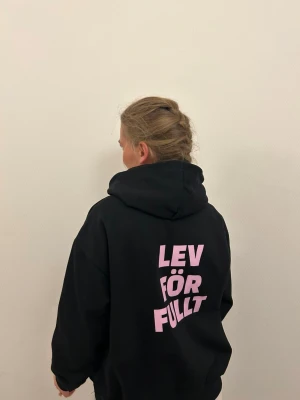 Svart hoodie med rosa tryck - Svart hoodie med  rosa text på ryggen som säger ”LEV FÖR FULLT”
