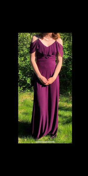 Balklänning - Elegant lila långklänning i ett mjukt och flödande material med inbyggd bh. Klänningen har en v-ringad design med offshoulder-ärmar och vackra draperade detaljer framtill. Perfekt för en speciell kväll, festlig tillställning eller bal. Använd 1 gång, pris kan diskuteras.
