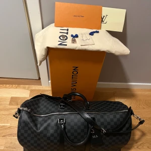 Louis Vuitton Keepall 55 Damier Graphite - Knappt använt min bag, den är som ny, har kanske 1-4 märken på den men de är knappast synliga. Kommer med allt, nycklarna, nyckellåset, dustpåsen till nycklarna, dustpåsen till väskan, boxen, brevet med kvitteringen. Köpt från LV butiken i Oslo.