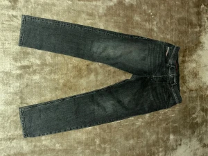 Diesel Jeans - Svartgråa Diesel jeans med klassisk straight fit och fem fickor. Jeansen har en något tvättad look och är tillverkade i slitstarkt denim. Passar dig som gillar tidlös stil och vill ha ett par jeans med ikonisk knappgylf. Jeansen är sparaamt använda, därav priset!