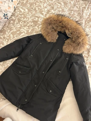 Svart Rockandblue parkas med pälskrage - Säljer en svart parkas från Rockandblue i storlek 38. Jackan har en stor fluffig pälskrage i brunt, dragkedja och knappar framtill samt praktiska fickor med lock. Perfekt för kalla vinterdagar och riktigt snygg streetstil.