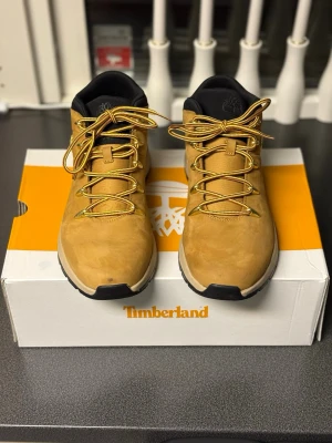 Timberland Sprint Trekker boots beige - Timberland Sprint Trekker boots i beige mocka med svarta detaljer och guldfärgade snörhål. Skorna har rund tå, platt sula och grova snören i gul/svart. Timberland-logga i guld på sidan och broderad logga på plösen. Perfekt för dig som gillar street och outdoor. Ett litet märke på ena tån men man tänker it på de när det är snö och dom är perfekt nu till vintern.
