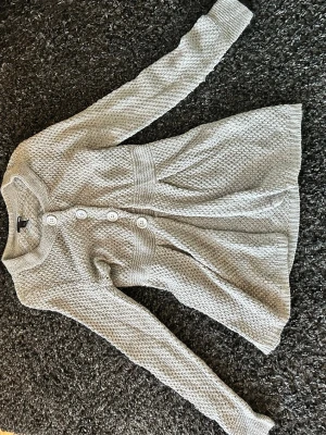 Grå stickad kofta med knappar - Mysig grå stickad kofta från H&M med lång ärm och stora vita knappar framtill. Koftan har en lätt utställd passform och ribbade muddar vid ärmslut och nederkant. Perfekt för lager-på-lager under kyliga dagar.