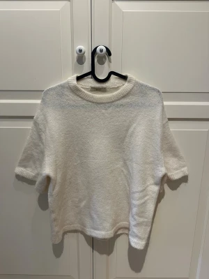 Vit stickad tröja från Gina Tricot  - Säljer en vit stickad tröja från Gina Tricot med korta ärmar och rund hals. Tröjan har en mjuk och fluffig känsla. Använd ett fåtal gånger. 