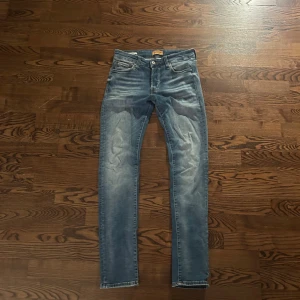 Blå Jack & Jones slim Glenn  - Snygga blå jeans med slim fit och klassisk femficksdesign. Jeansen har en lätt tvättad look med slitningar på framsidan och bakfickor. Perfekt passform och bekvämt material