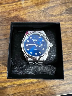 Silver clocka med blå urtavla - Stilren klocka med blå urtavla och silverfärgad jubilee länk i stainlessteel. Urtavlan har glittriga stenar som timmarkeringar, dag- och datumvisning samt en räfflad bezel. Klockan kan minskas både genom att ta ut länkar och minskas vid claspen. Klockan är icke använd! Priset kan diskuteras!