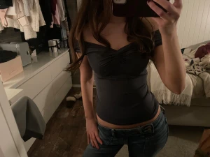 Mörkgrå offshoulder topp - Säljer en mörkgrå, tight offshoulder topp med snygg rynkning vid bysten. Toppen är croppad och har en smickrande passform som framhäver midjan. Perfekt för dig som gillar stilrena och trendiga plagg med lite edge.