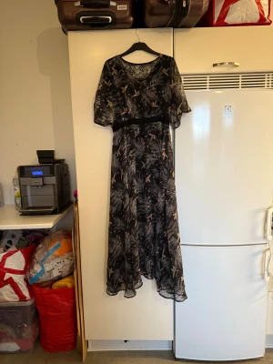 Svart långklänning med spets från Cream - Långklänning från Cream i svart med blommigt mönster och inslag av ljusa toner. Klänningen har korta ärmar, transparent spets upptill och ett luftigt, flowy tyg. Perfekt för dig som gillar romantiska detaljer och en bohemisk vibe. Storlek 38/M. Mycket fint skick, jag hittar inga synliga anmärkningar eller defekter. 